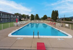 Relax by the clear pool surrounded by lounge chairs and umbrellas, with a low fence for safety.