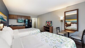 A hotel room with two beds, a kitchenette, a television, and a mirror.