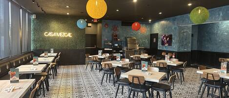 A restaurant interior with multiple tables and chairs, a neon sign reading "CASAMEZGAL", and a patterned floor.