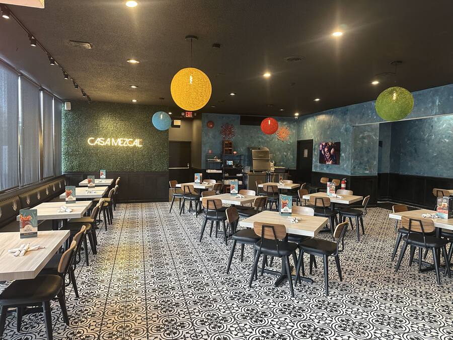 Interior de restaurante con varias mesas y sillas, un letrero de neón que dice 'CASAMEZGAL', y un suelo con diseño.