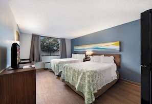 A hotel room with two beds, a desk with a television, and a painting on the wall.