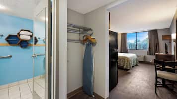 A hotel room with a shower, a bed, a desk, and a view of the outdoors.