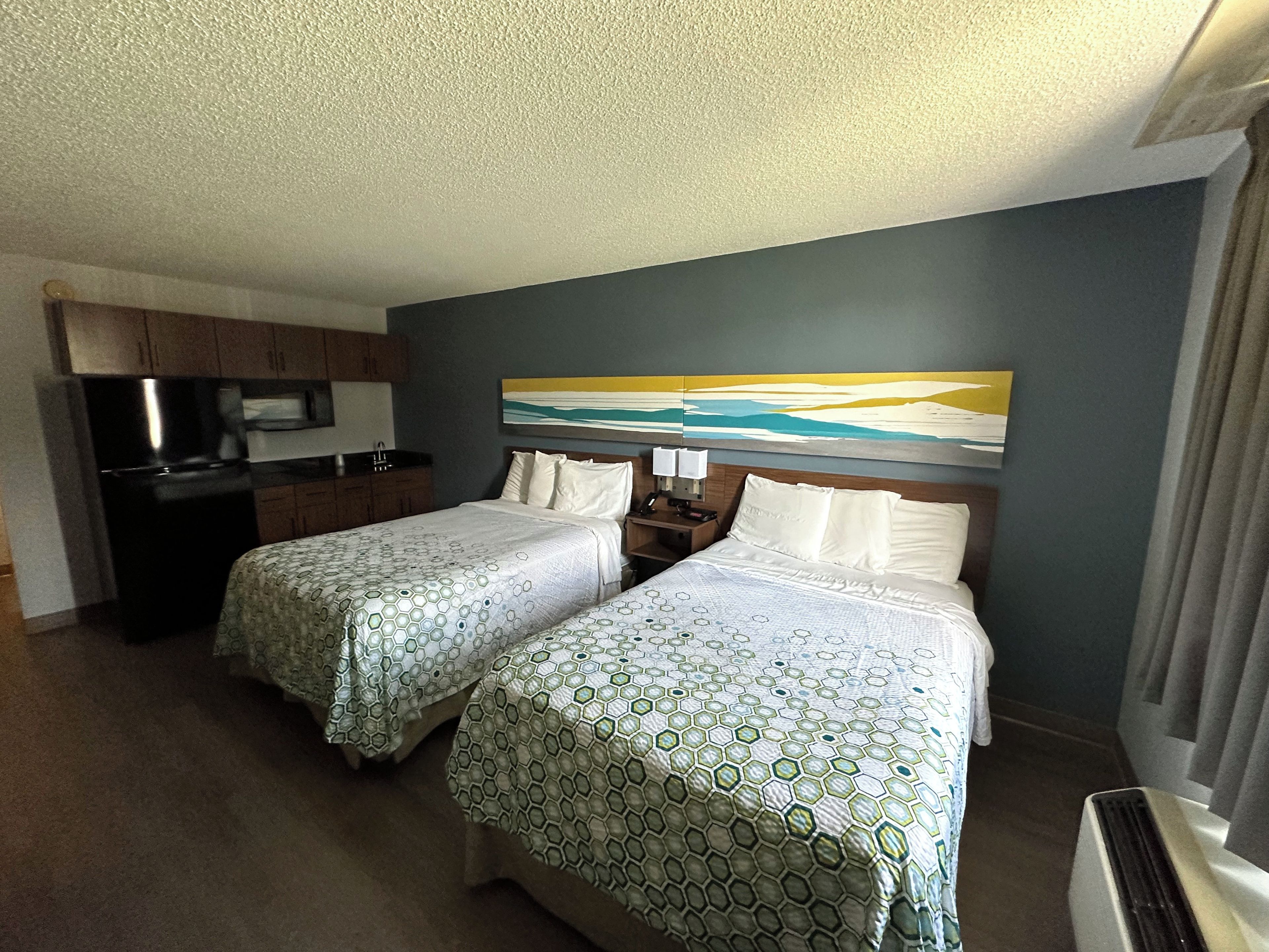 Une chambre d’hôtel avec deux lits, une kitchenette et un tableau au mur.