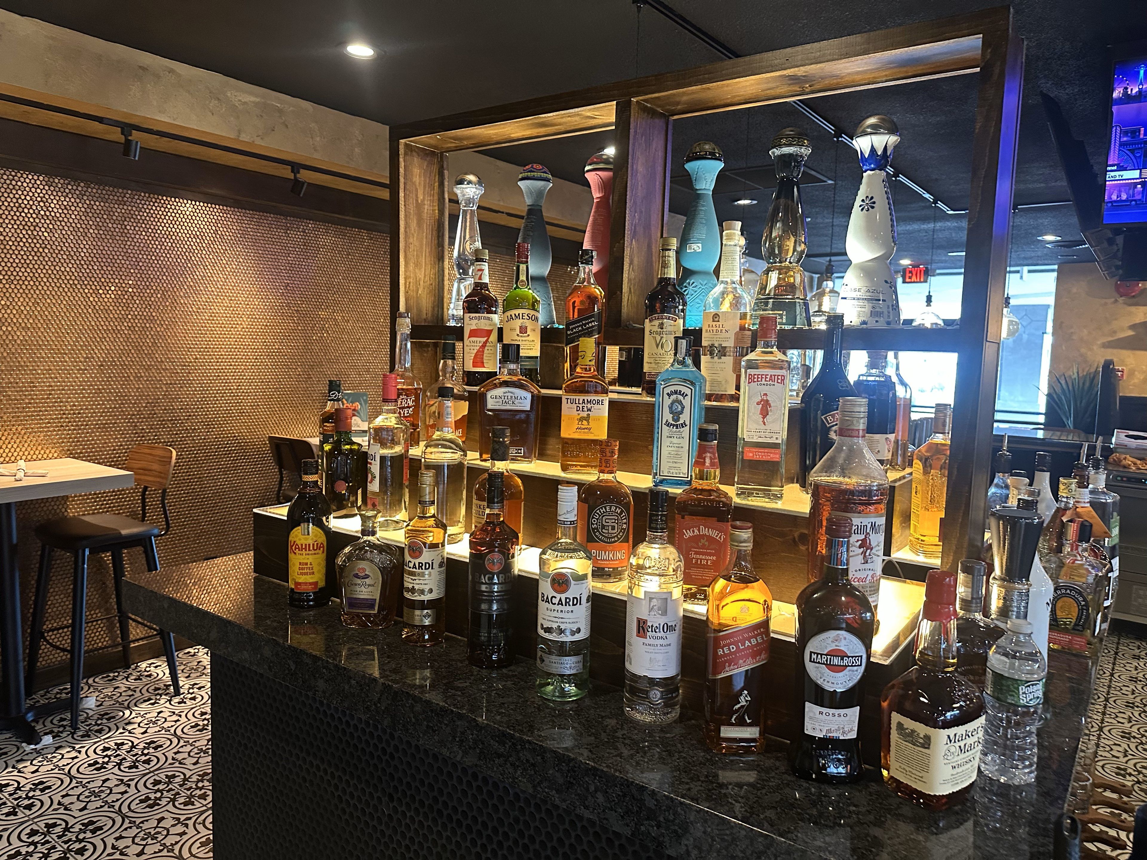 Zona de bar con una variedad de botellas de licores y una pantalla de televisión al fondo.