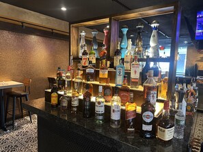 A bar area with a variety of liquor bottles and a television screen in the background. - HomeTowne Studios by Red Roof Painted Post (Painted Post)