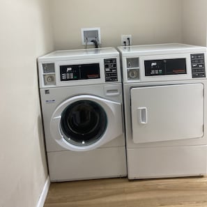 Two stacked front-loading washing machines with digital displays, a power outlet, and a wall-mounted electrical outlet.