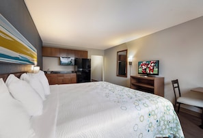 A hotel room with a bed, a television, a kitchen area, and a seating area.