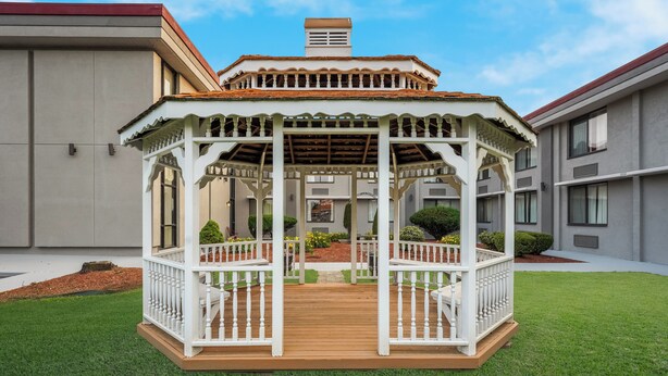 A gazebo with a wooden deck and white railings, surrounded by a well-maintained lawn and a building in the background.