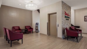 A reception area with a red carpet, a reception desk, a wall-mounted ATM, and a chandelier.