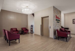 Un espace d’accueil avec un tapis rouge, un comptoir de réception, un distributeur automatique fixé au mur et un lustre.