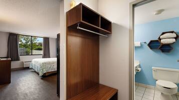 A hotel room with a bed, a wooden wardrobe, a bathroom with a toilet and towel rack, and a window with curtains.