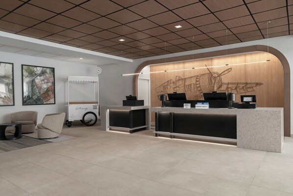 Zona de recepción de hotel con diseño moderno, que incluye un mostrador de recepción, un área de estar y obras de arte en las paredes.
