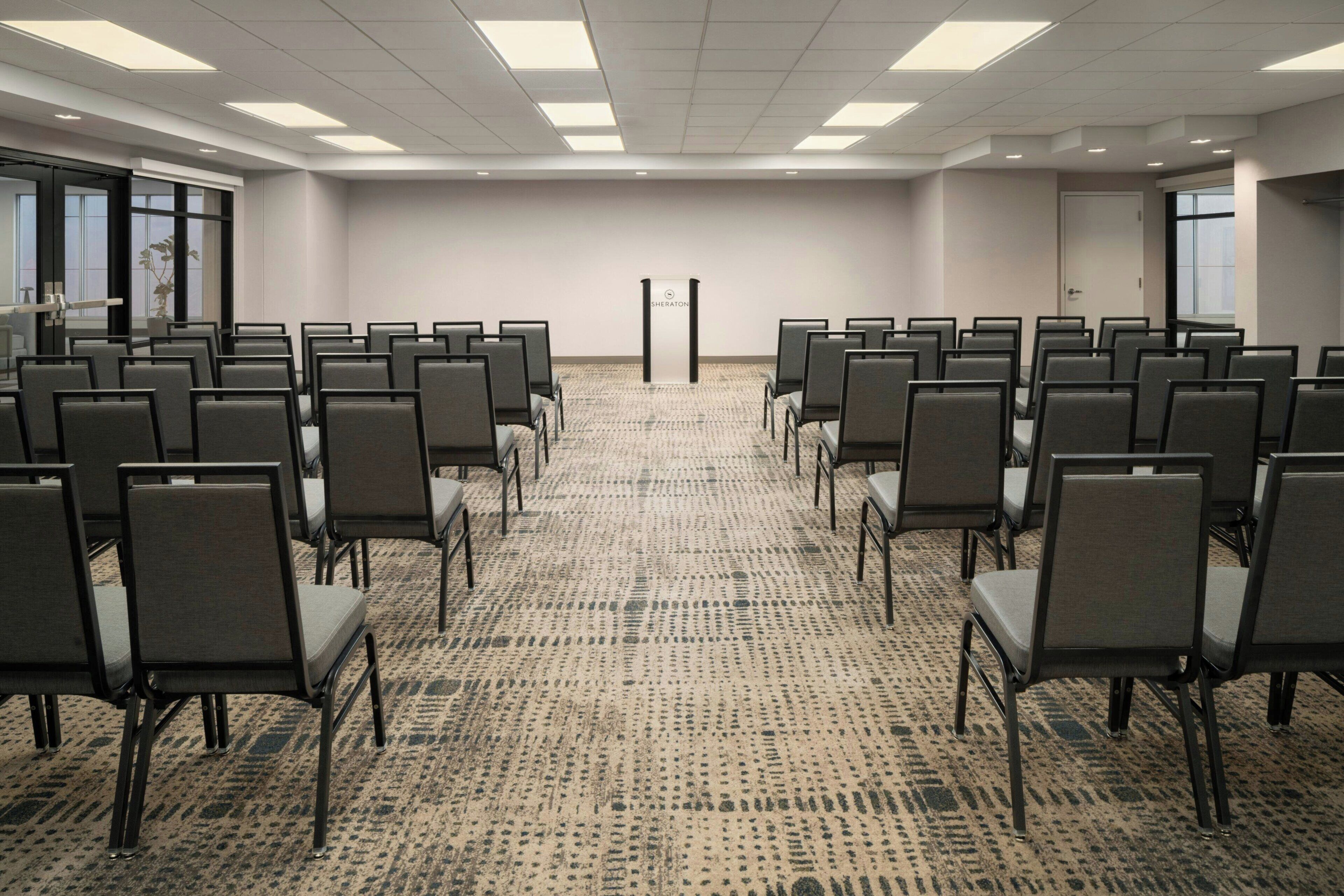 A conference room with rows of chairs, a carpeted floor, and a podium in the center.