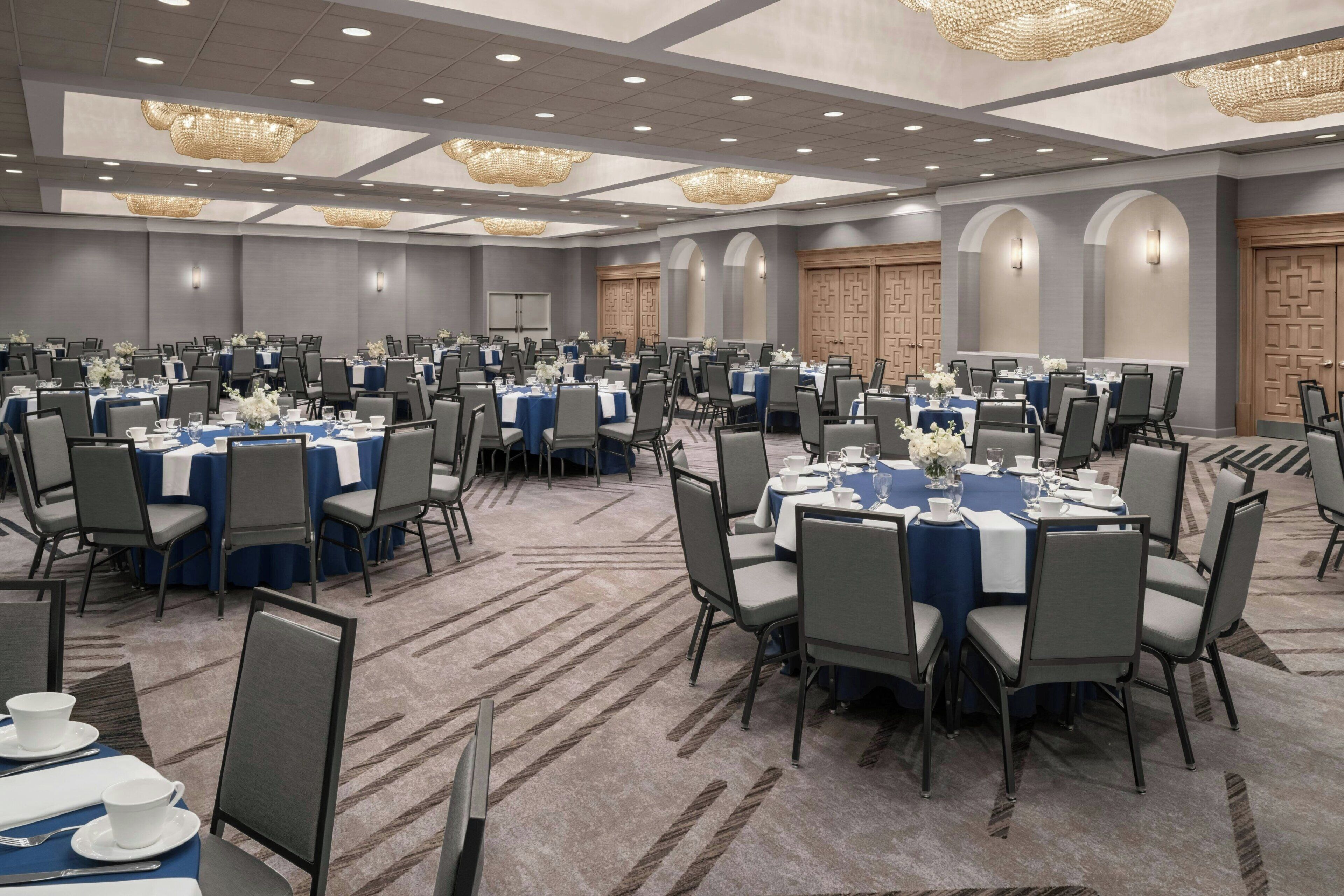 A large conference room with multiple tables and chairs, arranged in rows.