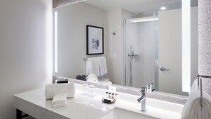 Ein modernes Badezimmer mit einem großen Spiegel, einem weißen Waschbecken und einer Duschkabine aus Glas.