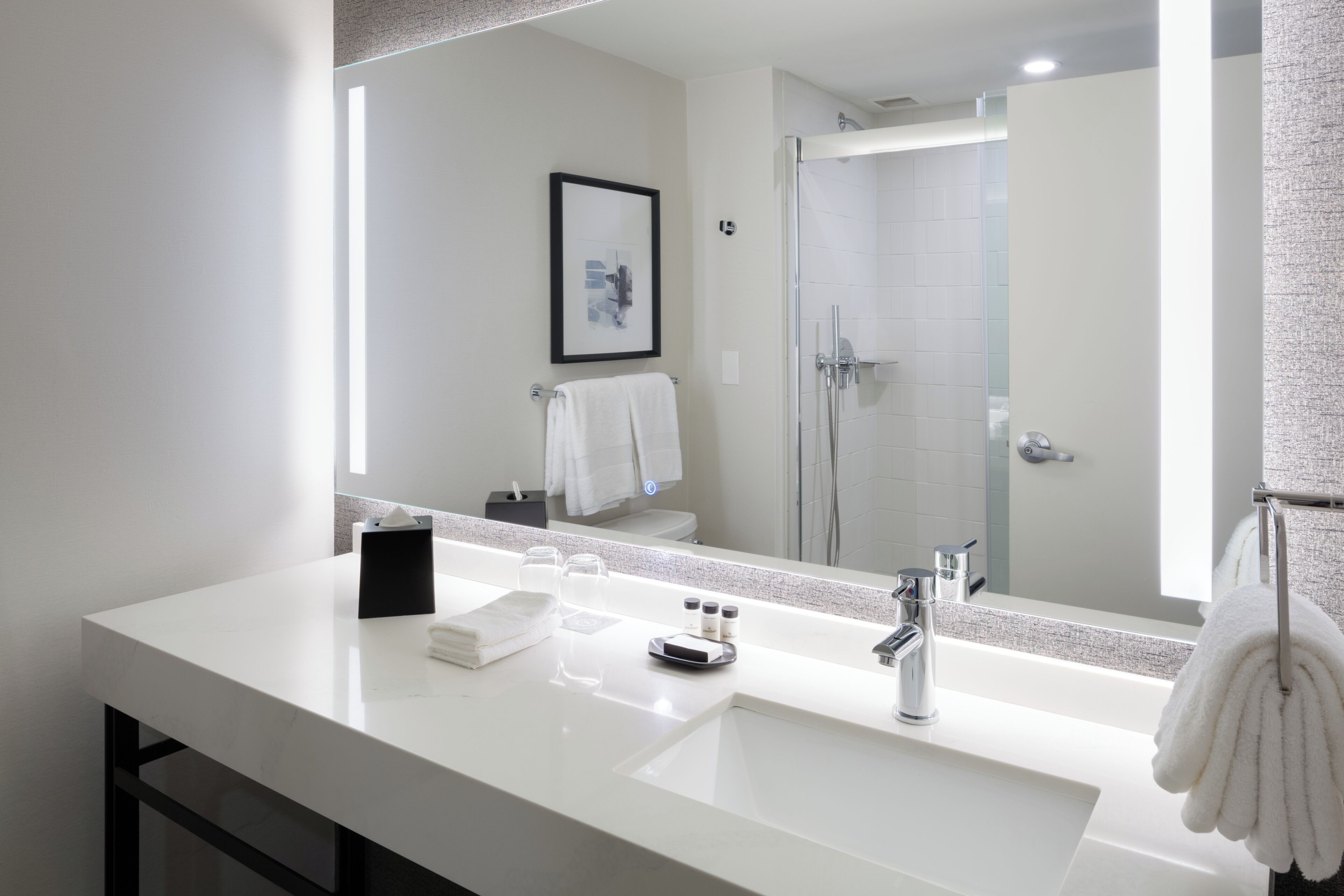 A modern bathroom with a large mirror, white sink, and a glass shower enclosure.