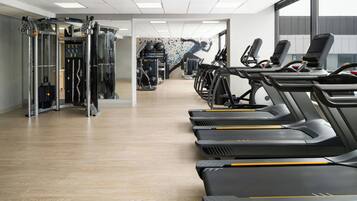 Un gimnasio con cintas de correr, máquinas de pesas y una pared decorada con un mural de temática fitness.