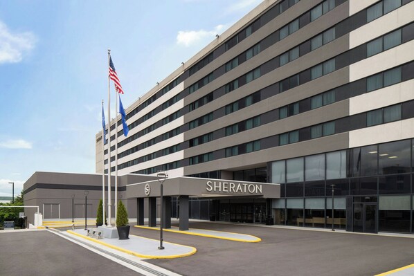 Un hotel Sheraton con fachada moderna, varios pisos y una entrada despejada.