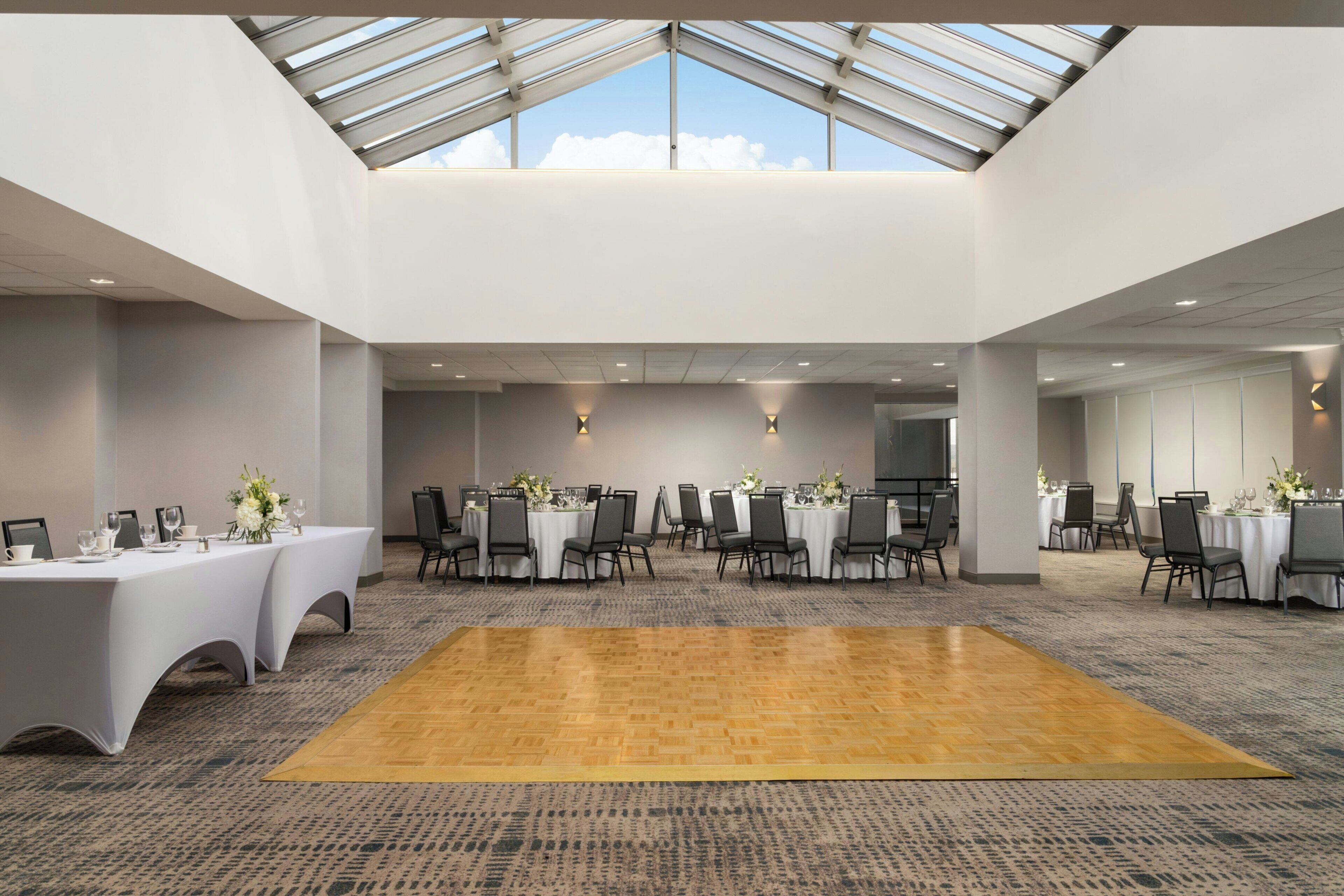 A large hall with a high ceiling and skylights, arranged with tables and chairs for events.