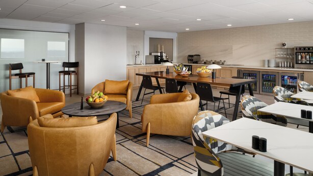 Un moderno vestíbulo de hotel con arreglos de asientos, una mesa de comedor central y una zona de kitchenette.