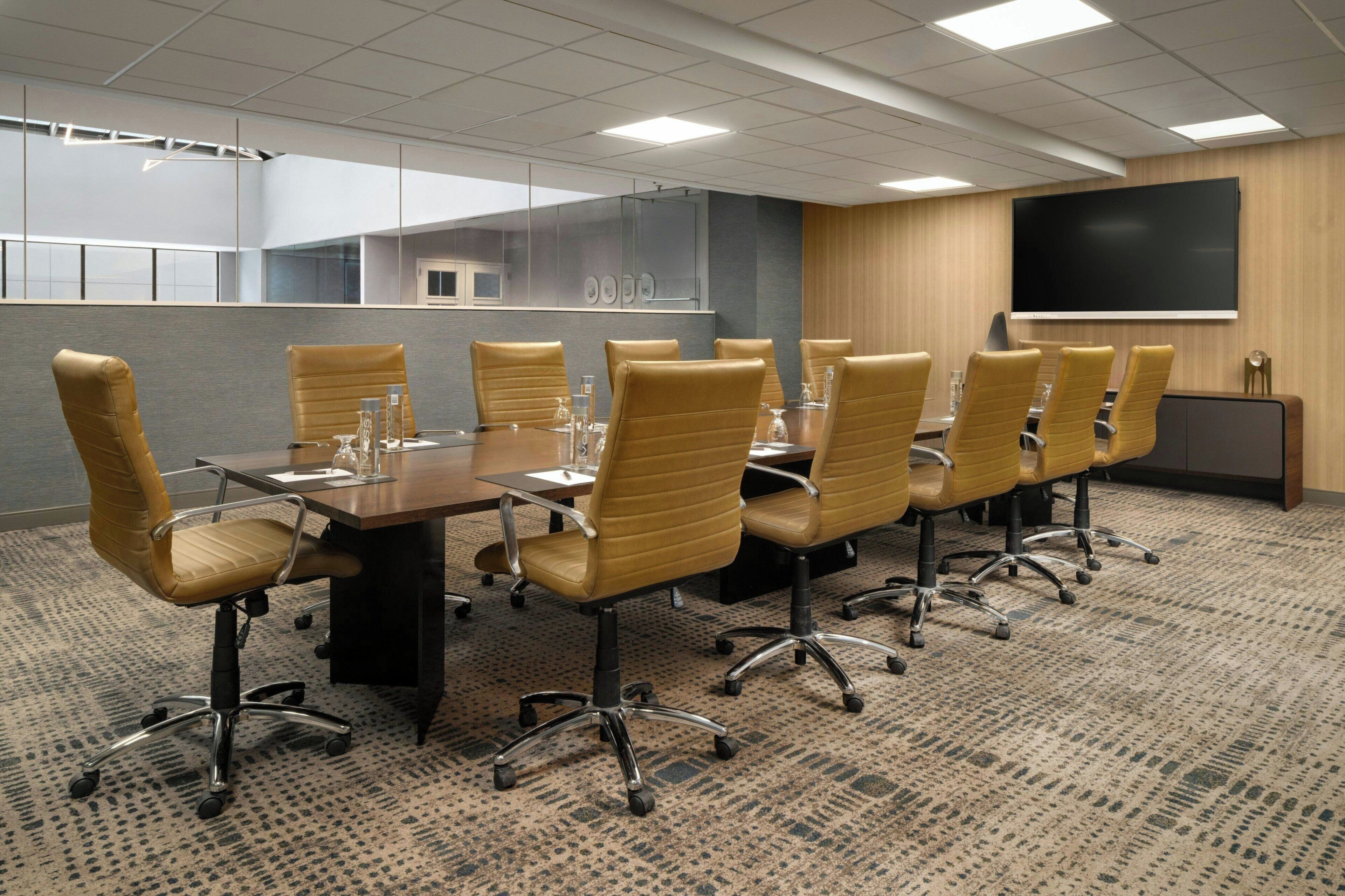 A conference room with a long table, multiple chairs, a projector screen, and a carpeted floor.