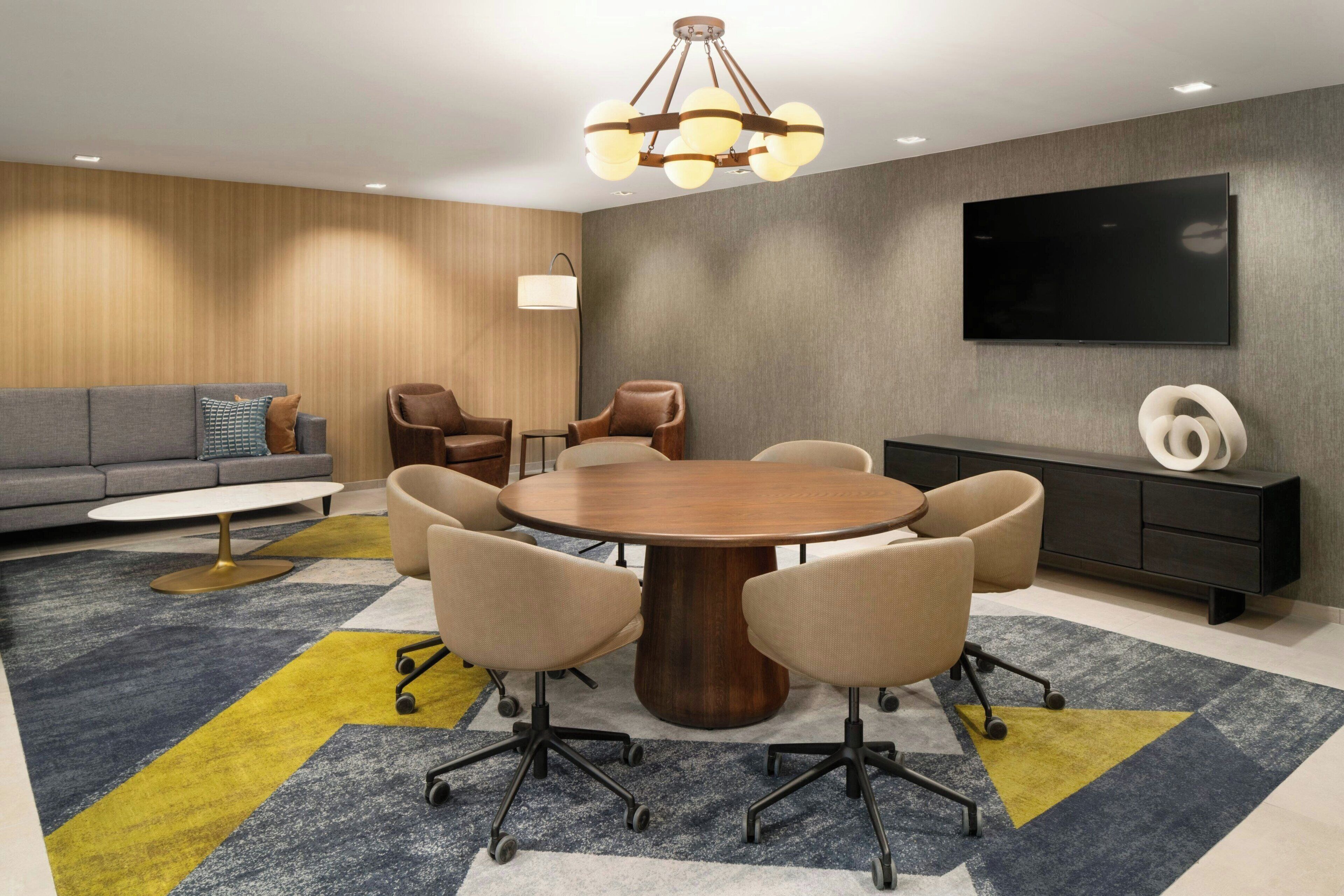 A modern conference room with a round table, chairs, a sofa, a TV, and a lamp.