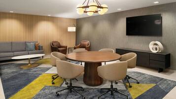 A modern conference room with a round table, chairs, a sofa, a TV, and a lamp.