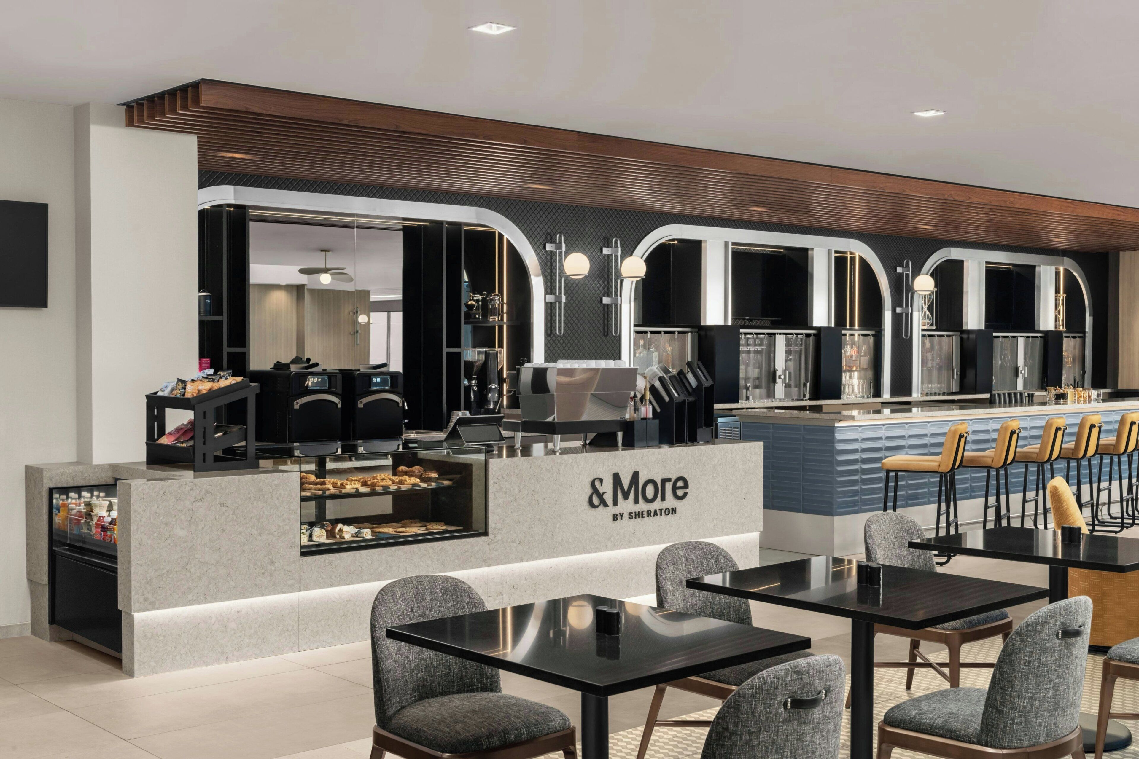 A modern cafe with a counter displaying pastries and a seating area with tables and chairs.