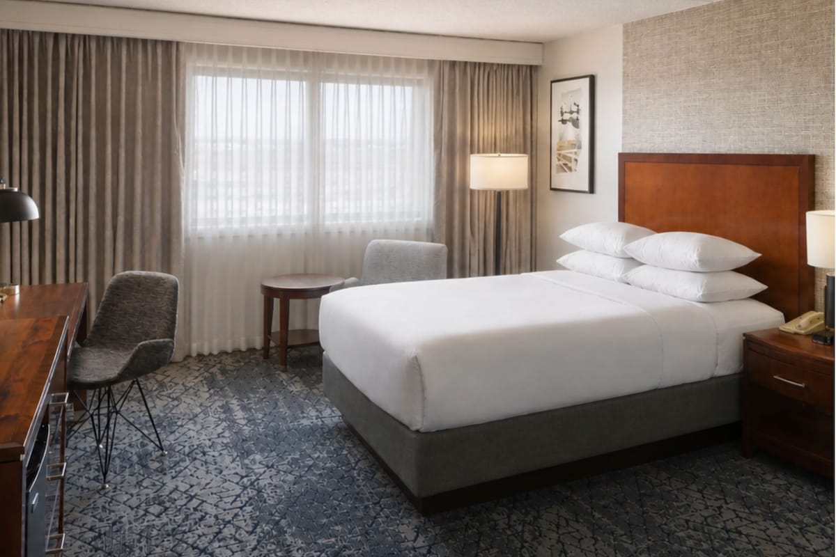Une chambre d’hôtel avec un grand lit, un bureau, une chaise, une petite table et une lampe.