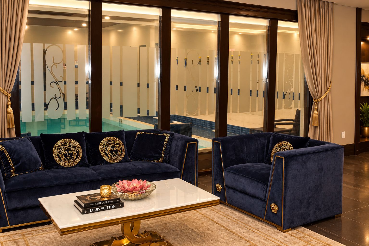 A luxurious living room with a sofa and armchair, a coffee table, and a view of an indoor pool.