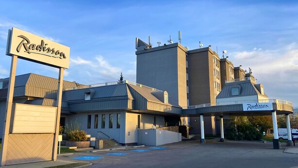 Un hotel Radisson con un diseño arquitectónico moderno, que incluye un letrero destacado, un área de estacionamiento y una entrada cubierta.