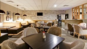 Un comedor moderno con cabinas y mesas, una pared de acento de piedra y un televisor de pantalla plana montado en la pared.