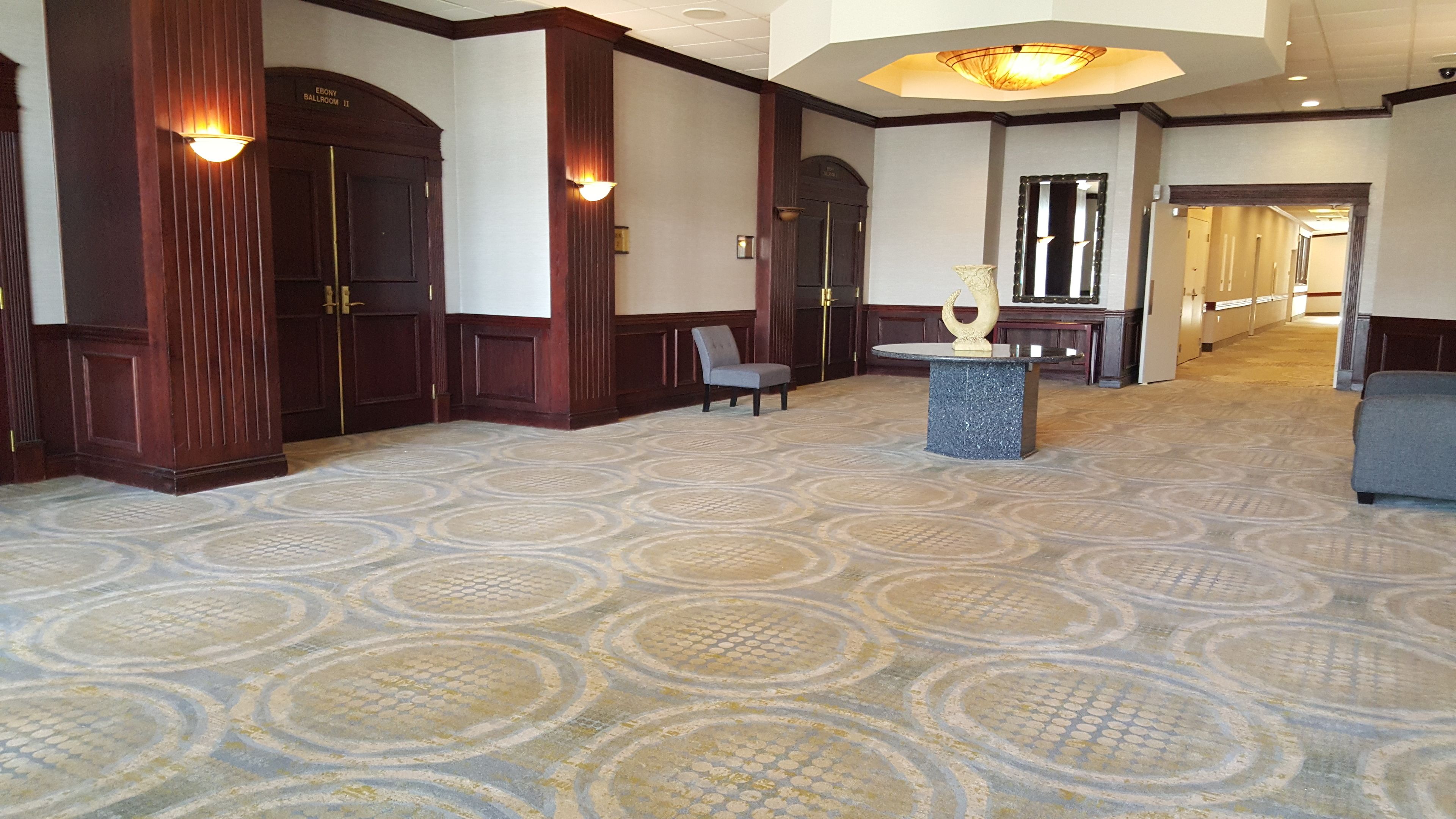 A spacious lobby with a patterned carpet, wooden paneling, and a chandelier.
