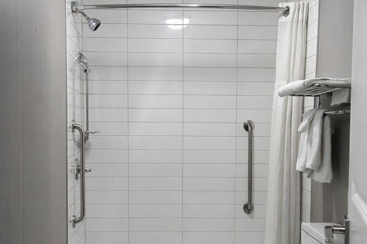 Une salle de bain moderne dotée d’une douche à l’italienne, de barres d’appui, de toilettes et d’un porte-serviettes.