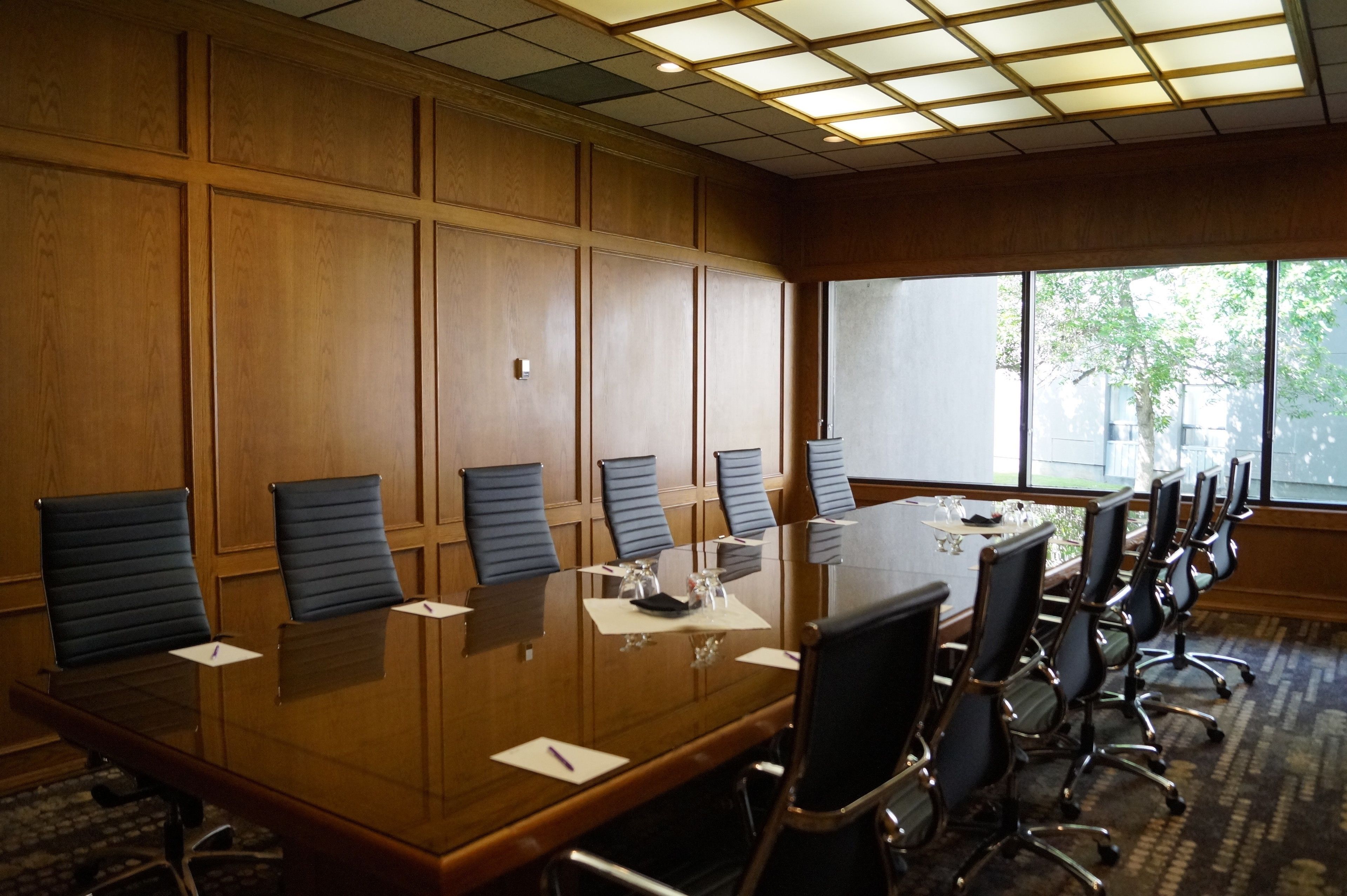 A conference room with a long table, multiple chairs, and a large window providing natural light.