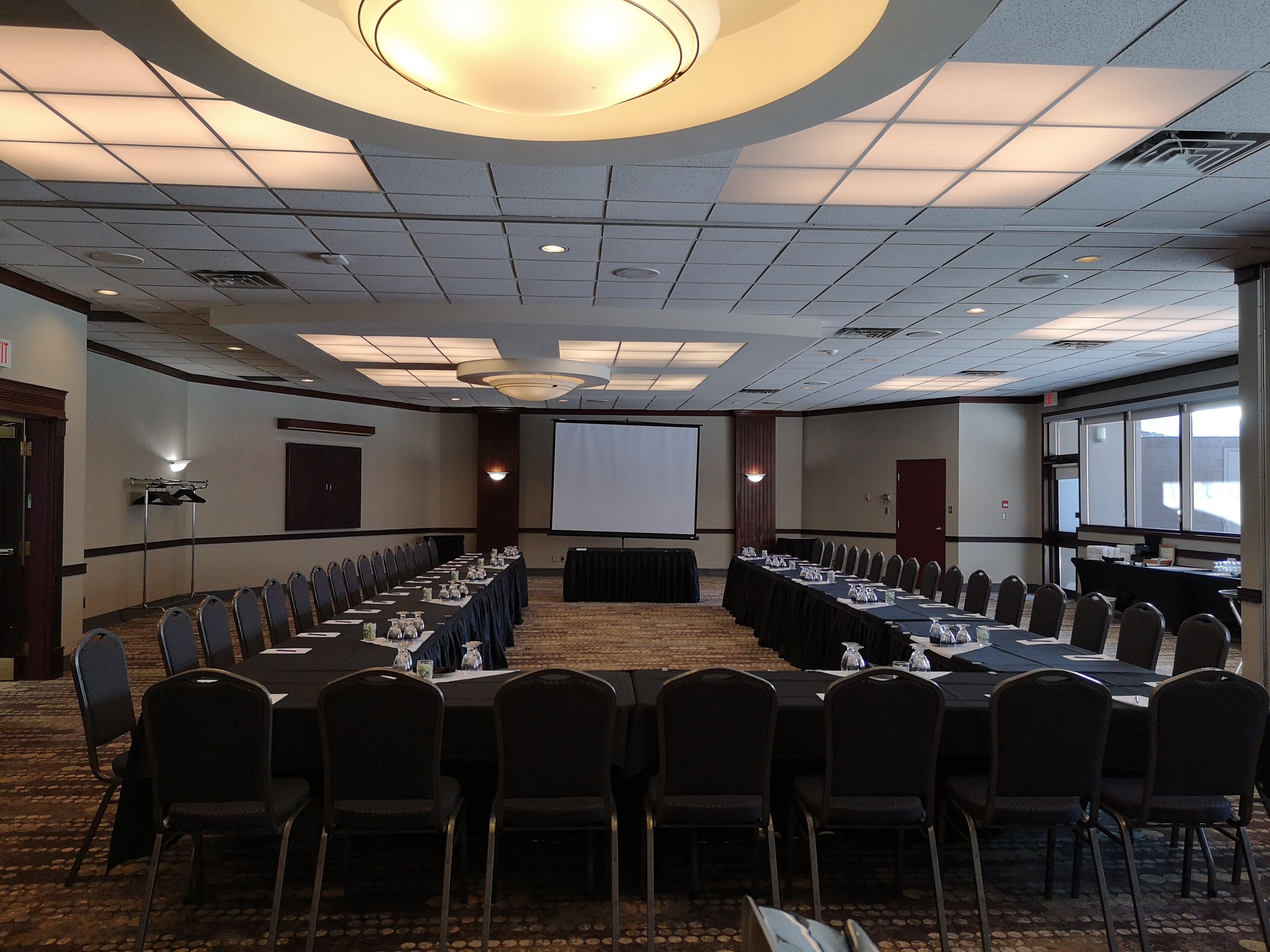 A conference room with a long table, chairs, a projector screen, and a carpeted floor.