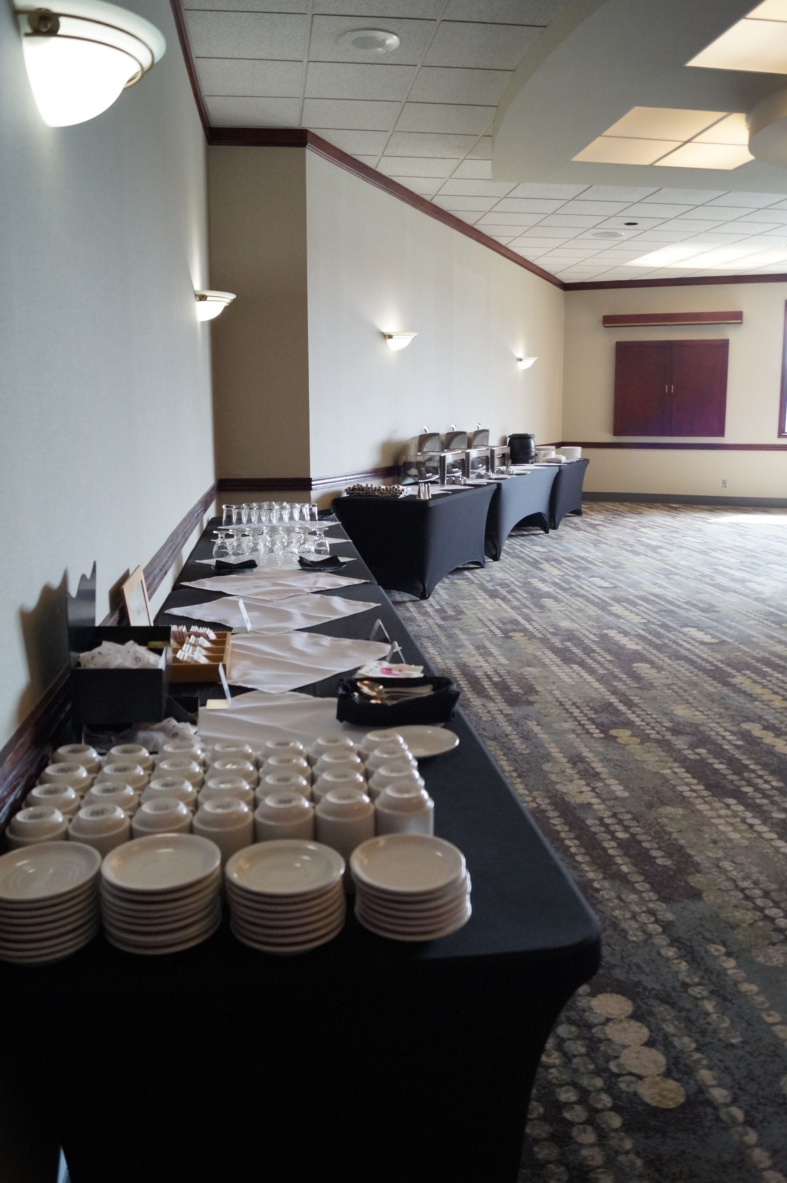 Una mesa de banquete dispuesta con platos, vasos y una estación de buffet en una habitación de hotel.