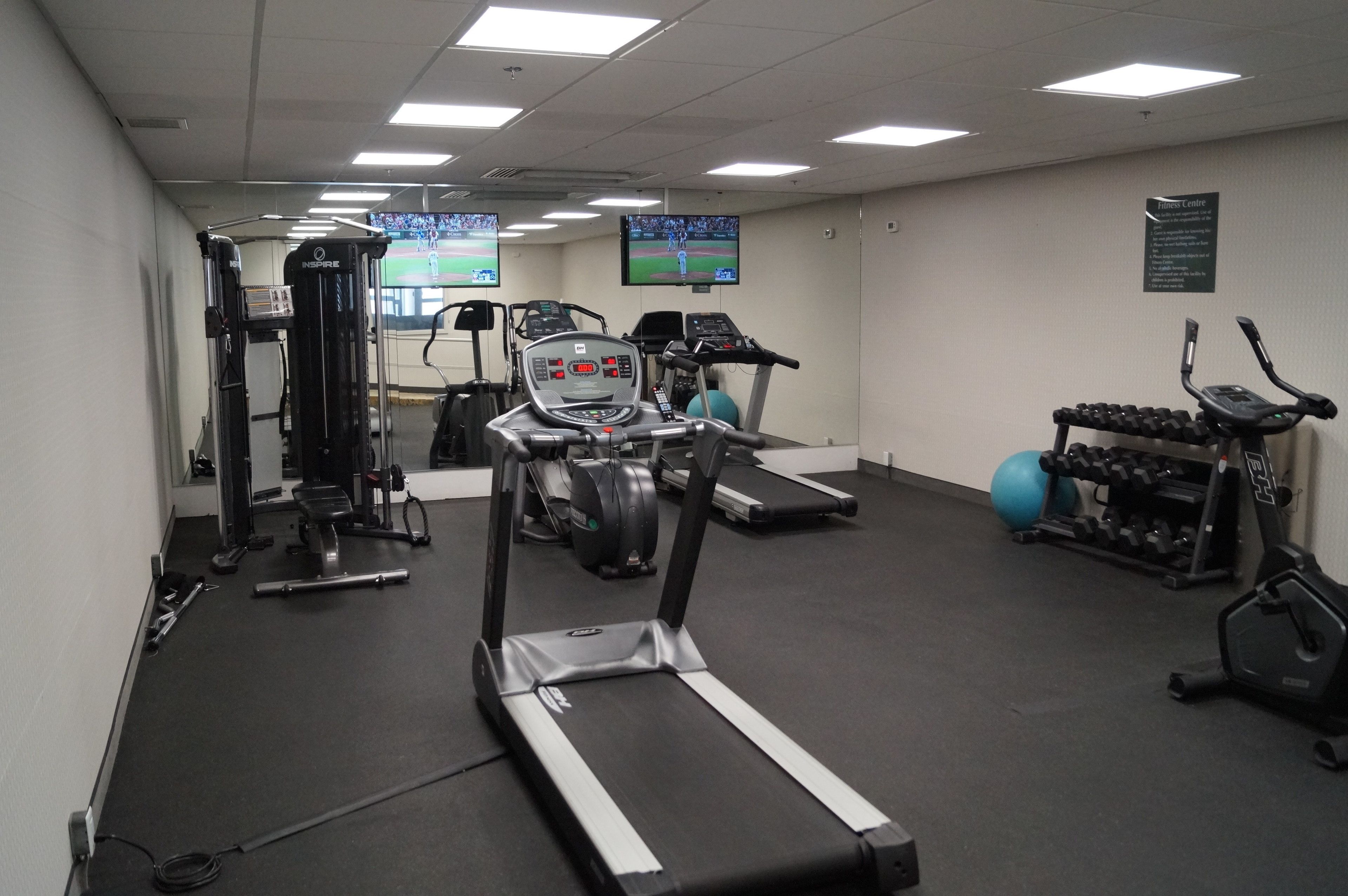 Une salle de sport équipée de tapis de course, d’appareils de musculation et de ballons d’exercice.