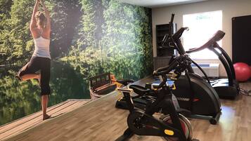 Ett gym med en motionscykel, en crosstrainer och en yogamatta på ett trädäck.