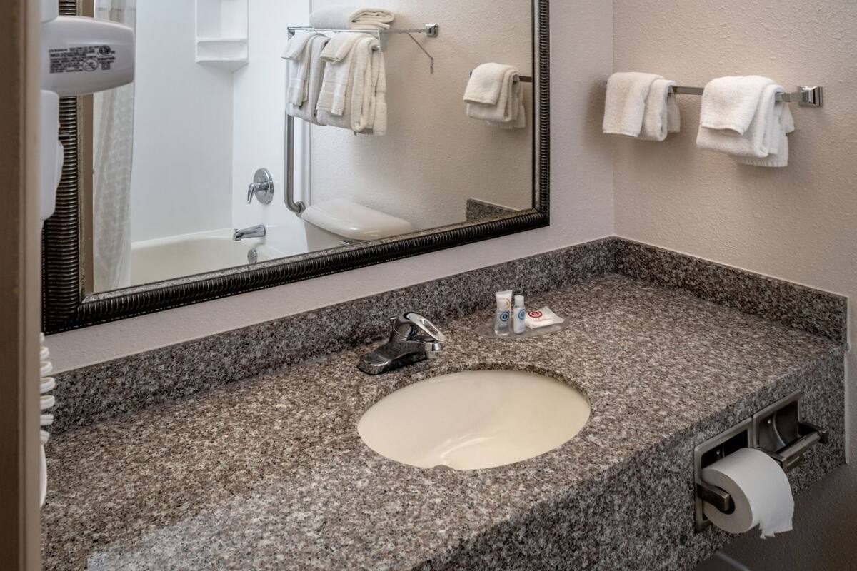 A bathroom with a granite countertop, a sink, a mirror, and a towel rack.
