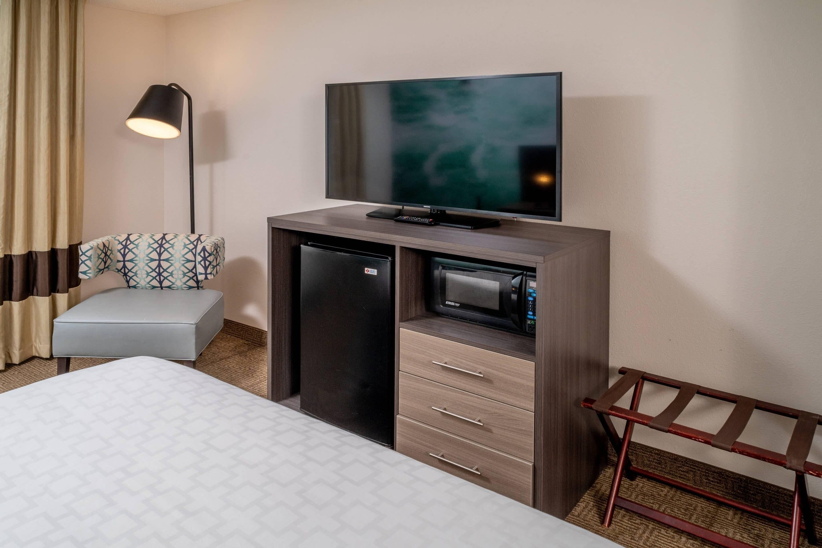 A hotel room with a bed, a desk with a flat-screen TV, a microwave, and a small refrigerator.
