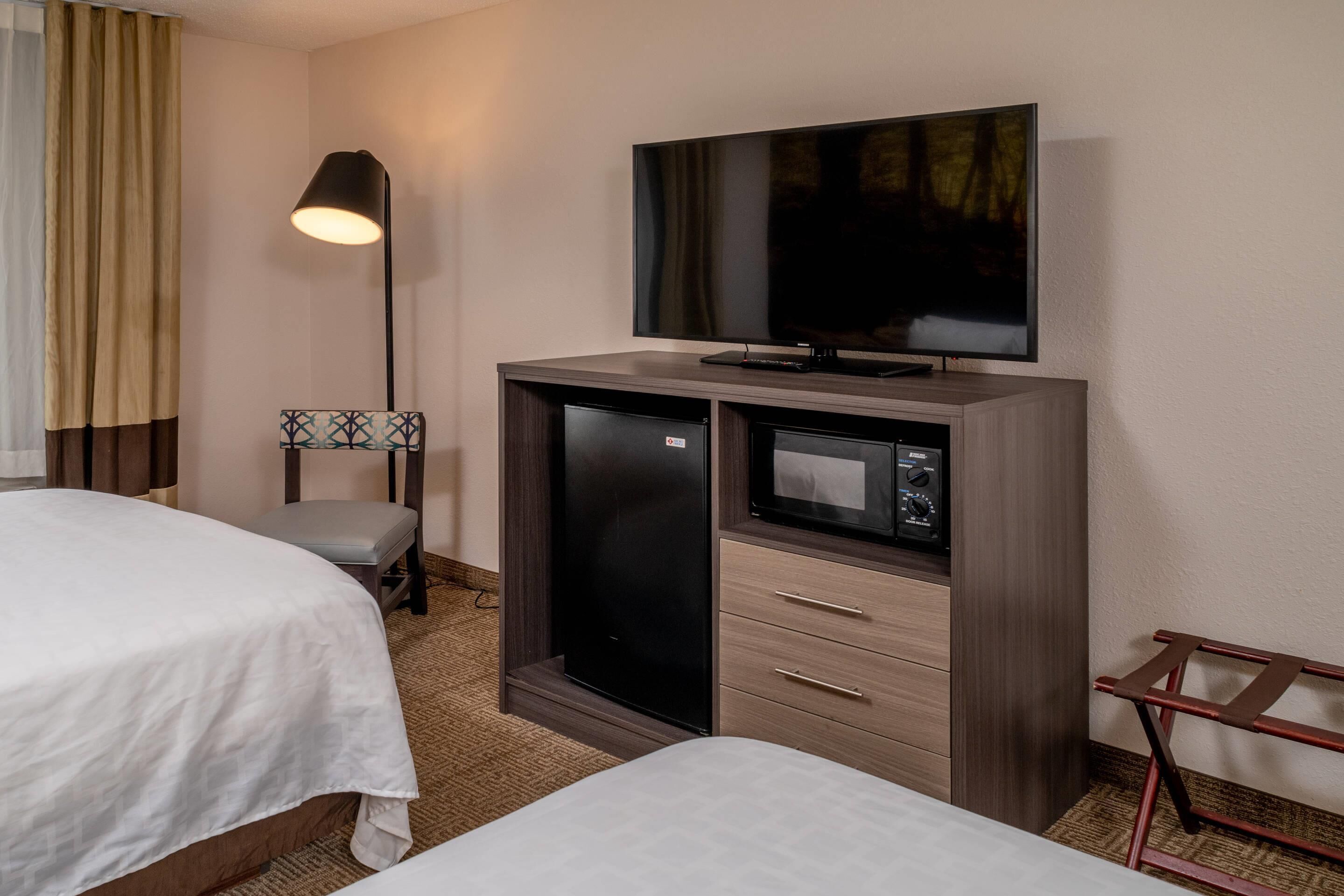 A hotel room with two beds, a flat-screen TV, a minibar, and a desk lamp.