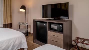 A hotel room with two beds, a flat-screen TV, a minibar, and a desk lamp.