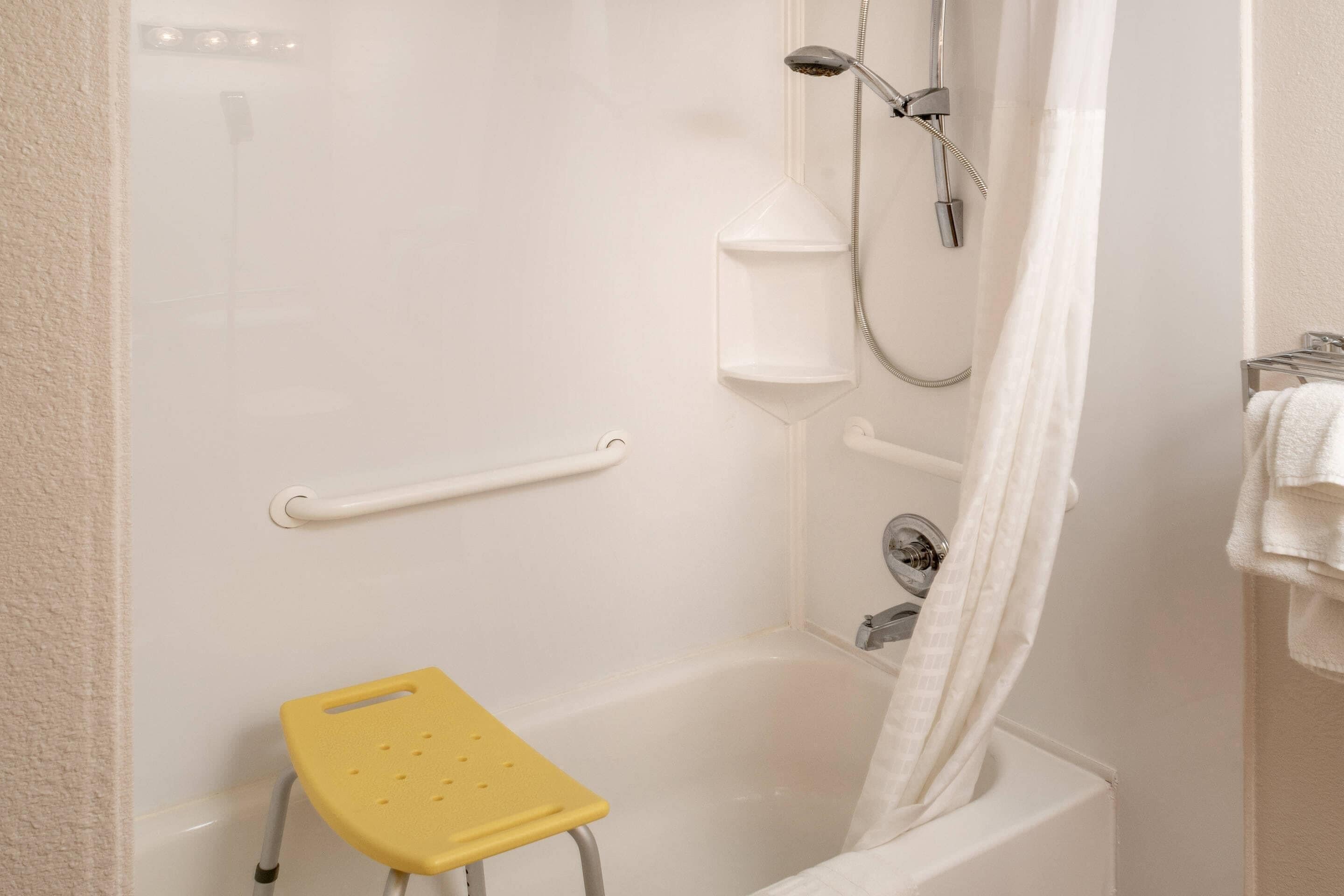 Une salle de bain avec une baignoire, une douche, un porte-serviettes blanc, un rideau de douche blanc et un petit tabouret jaune.