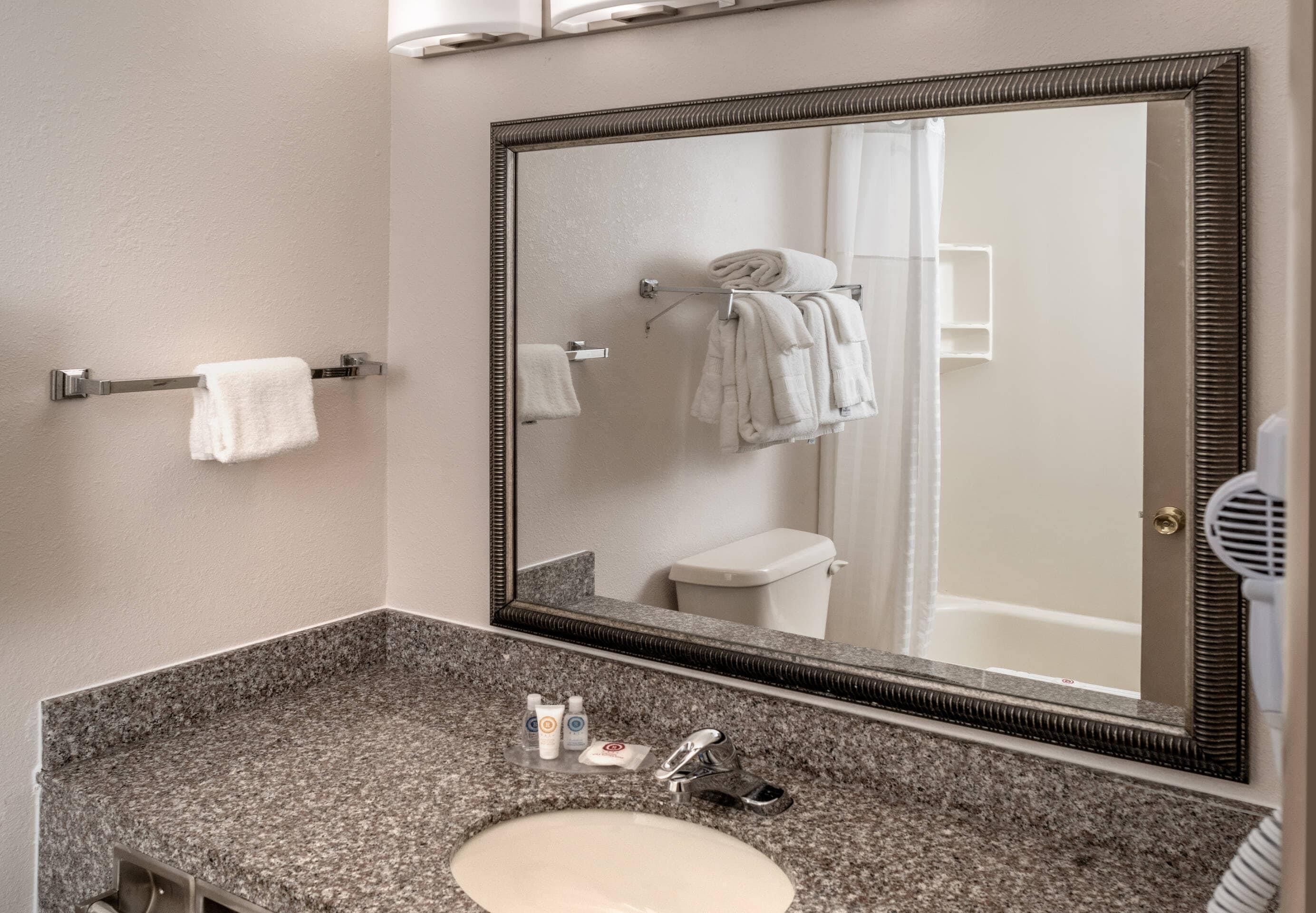 A bathroom with a granite countertop, a white sink, a large mirror, and a towel rack with towels.