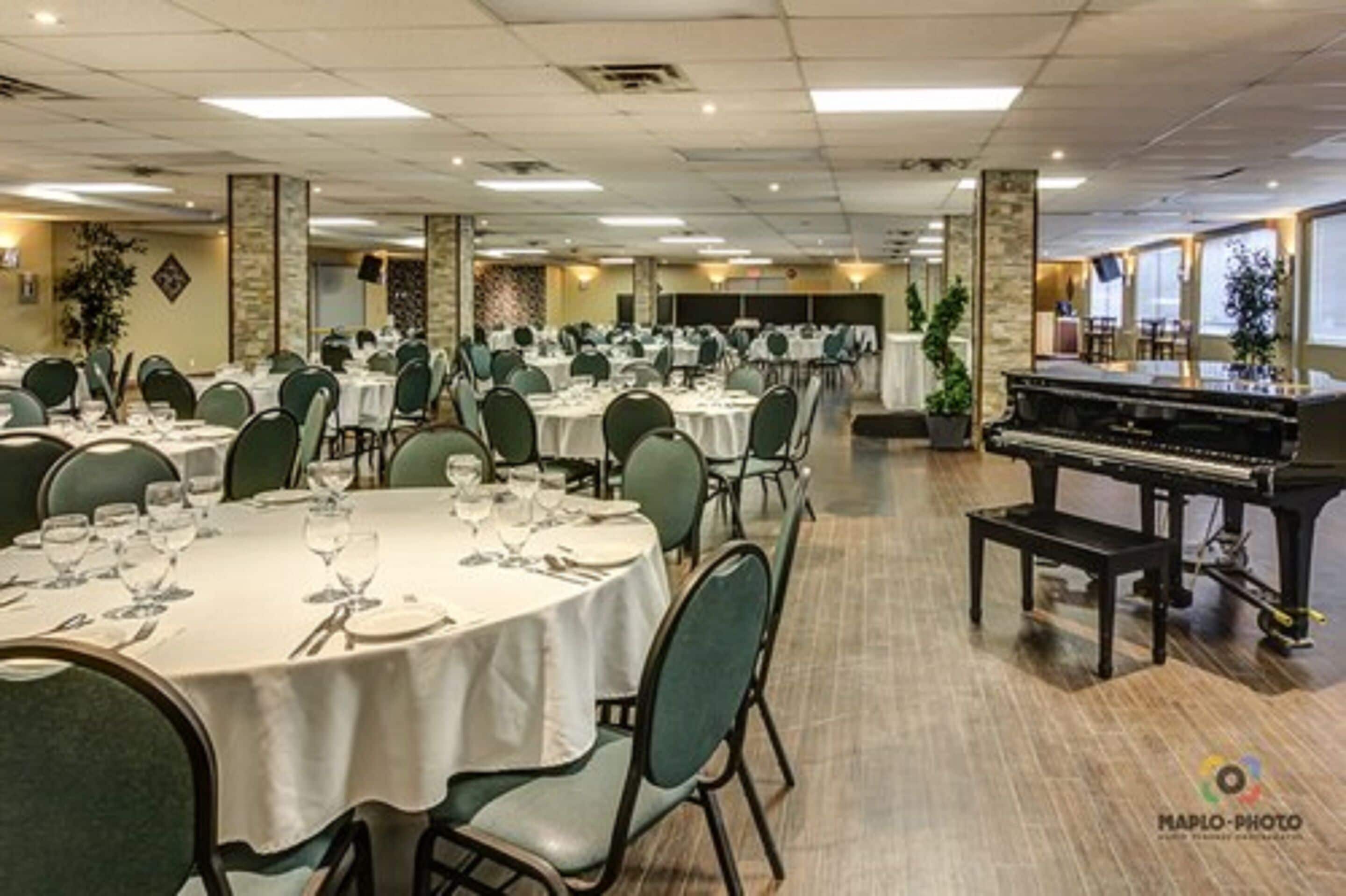 Une salle de banquet avec des tables rondes dressées pour le repas, un piano et une scène.