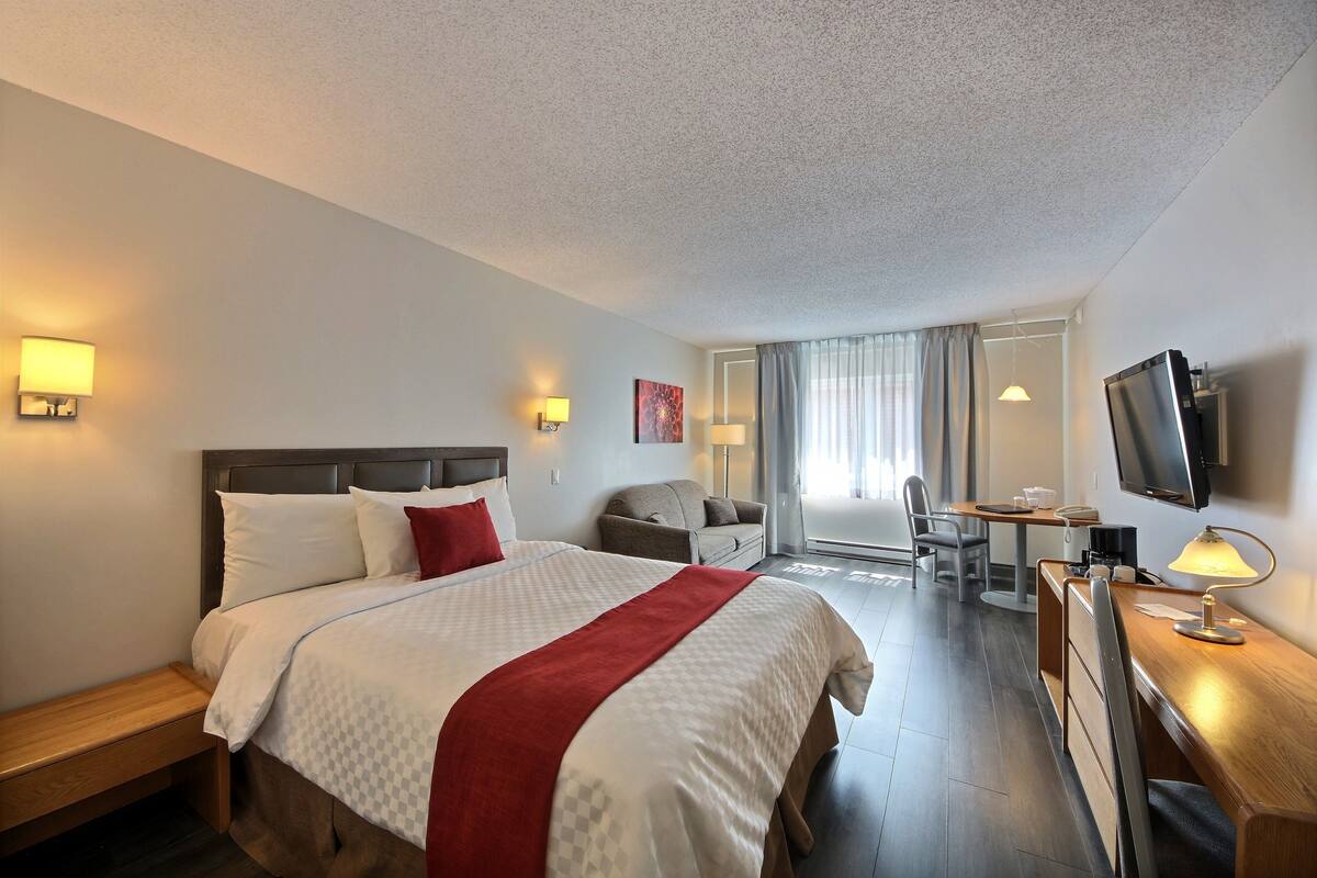 A hotel room with a bed, bedside table, TV, desk, and seating area.