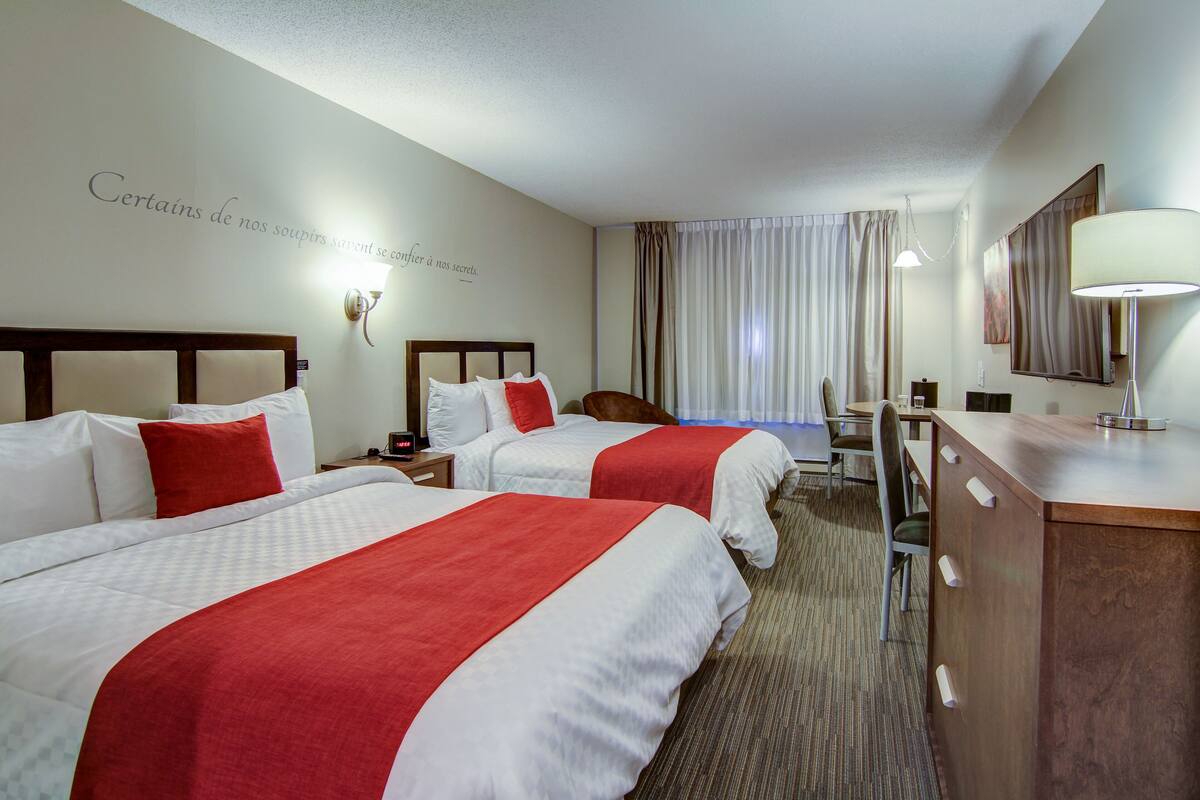 A hotel room with two beds, a desk, a chair, a lamp, and a mirror.