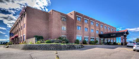 A multi-story hotel with a brick facade, a covered entrance, and a parking lot.
