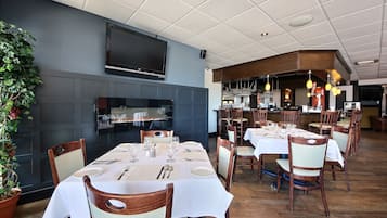 Ein Restaurant mit mehreren gedeckten Tischen, einem großen Flachbildfernseher an der Wand und einem sichtbaren Barbereich im Hintergrund.